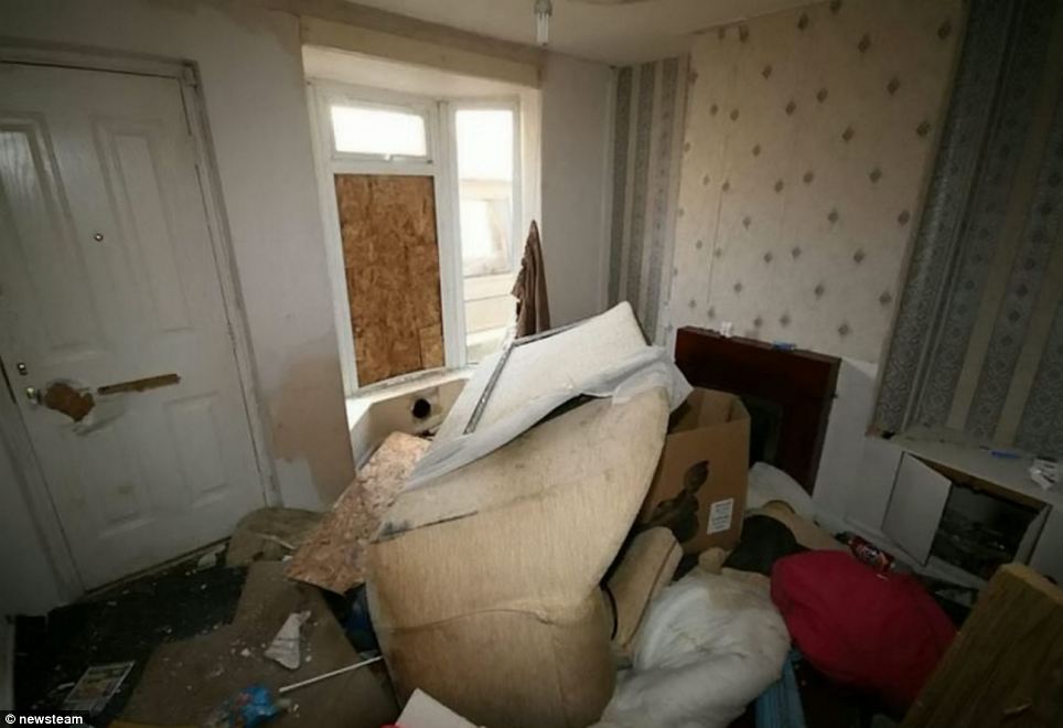The front-facing living room of the terraced house - which comes complete with boarded-up windows, an upturned sofa and piles of rubbish